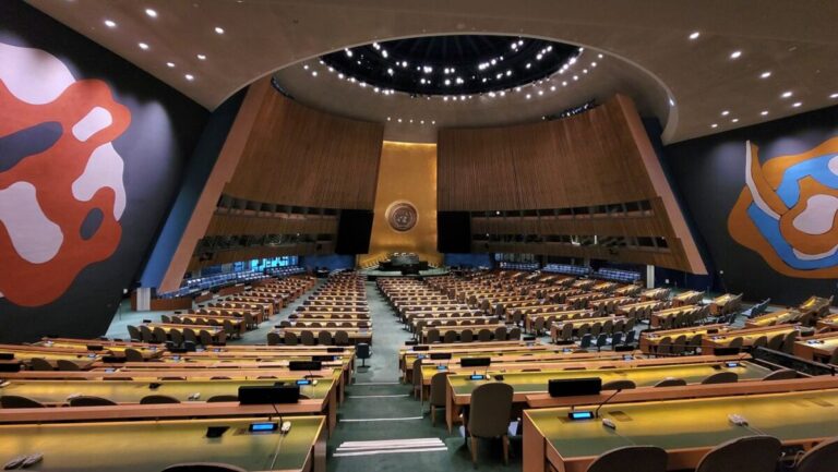 Plenário da Assembleia-Geral da ONU, em Nova York, visto de cima, com as fileiras de mesas e o emblema ao fundo