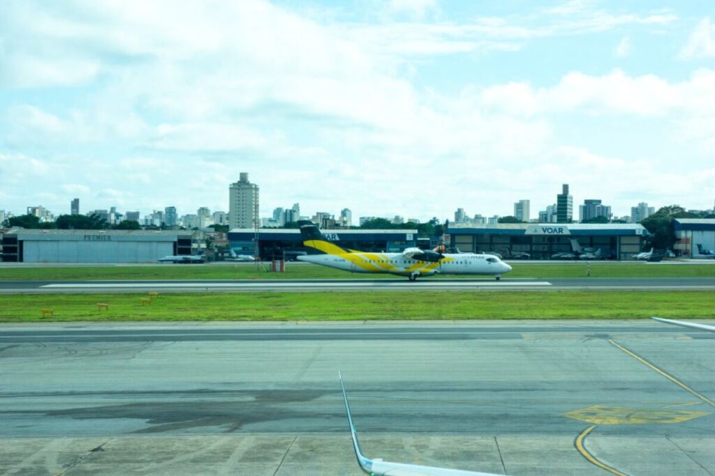 Avião ATR 72 da Voepass, amarelo e branco, em uma pista de aeroporto, com prédios da cidade ao fundo