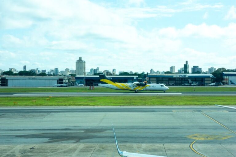 Avião ATR 72 da Voepass, amarelo e branco, em uma pista de aeroporto, com prédios da cidade ao fundo