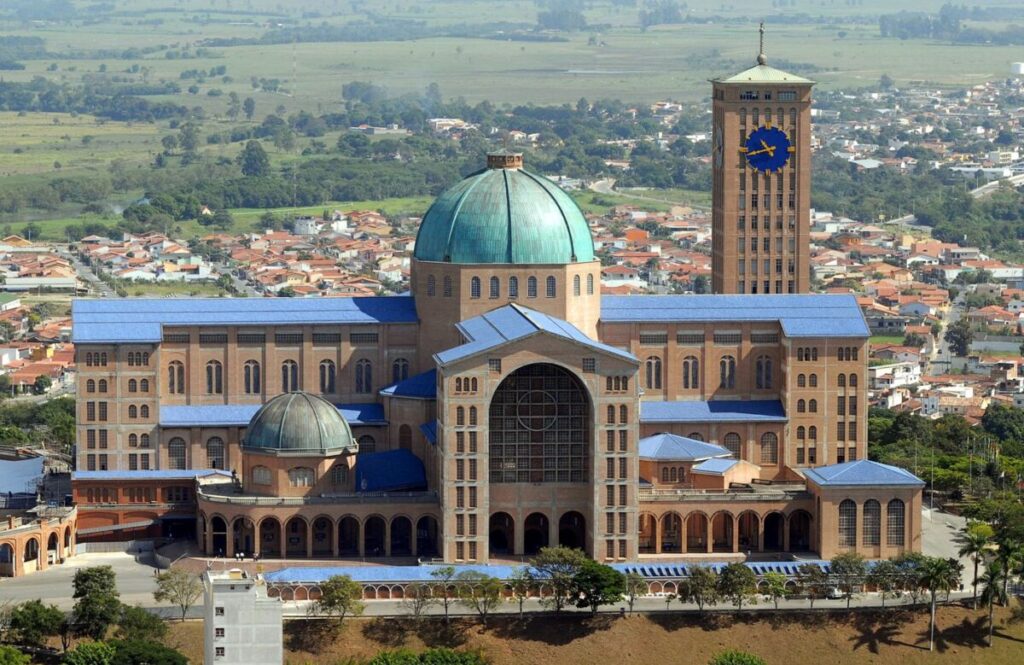 Vista aérea da Basílica Nacional de Nossa Senhora Aparecida, com a cúpula verde e a torre do relógio, cercada pela cidade de Aparecida (SP)