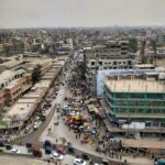 Vista aérea de uma rua movimentada no centro de Peshawar, com prédios, carros e riquixás
