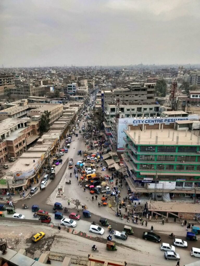 Vista aérea de uma rua movimentada no centro de Peshawar, com prédios, carros e riquixás