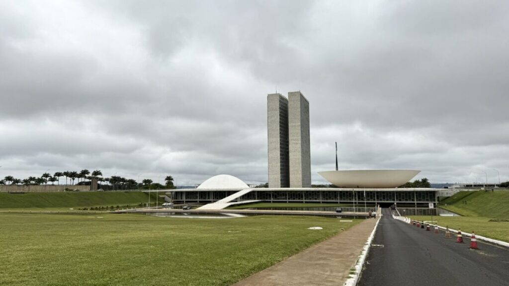 Vista do Congresso Nacional, com as duas torres e as cúpulas, sob céu nublado, em Brasília