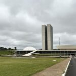 Vista do Congresso Nacional, com as duas torres e as cúpulas, sob céu nublado, em Brasília