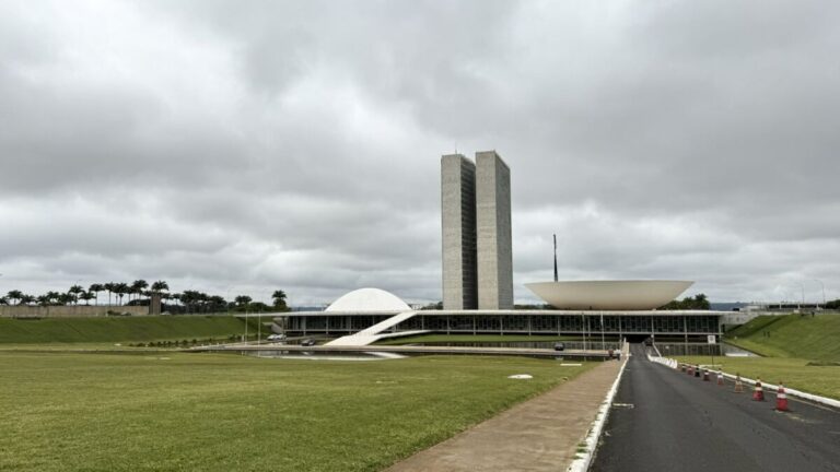 Vista do Congresso Nacional, com as duas torres e as cúpulas, sob céu nublado, em Brasília