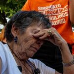 Mulher idosa com os olhos fechados e a mao na testa, cercada por manifestantes com camisetas do Sindicato de Inquilinas e Inquilinos de Madrid, durante protesto pela crise de moradia na Espanha.