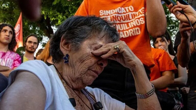 Mulher idosa com os olhos fechados e a mao na testa, cercada por manifestantes com camisetas do Sindicato de Inquilinas e Inquilinos de Madrid, durante protesto pela crise de moradia na Espanha.