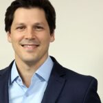 Retrato do governador de Goiás, Daniel Vilela, sorrindo, ao lado de uma bandeira