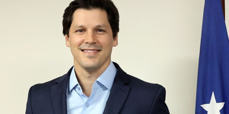 Retrato do governador de Goiás, Daniel Vilela, sorrindo, ao lado de uma bandeira