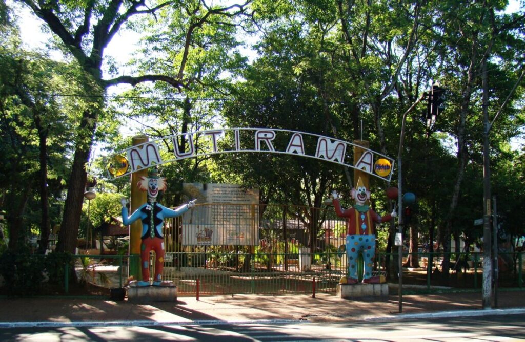 Entrada do Parque Mutirama, em Goiânia, com o arco com o nome do parque e dois bonecos de palhaço, cercada de árvores