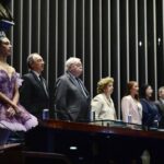 Bailarina de tutu roxo e coroa em pé, ao lado de autoridades em uma mesa, durante sessão especial no plenário do Senado