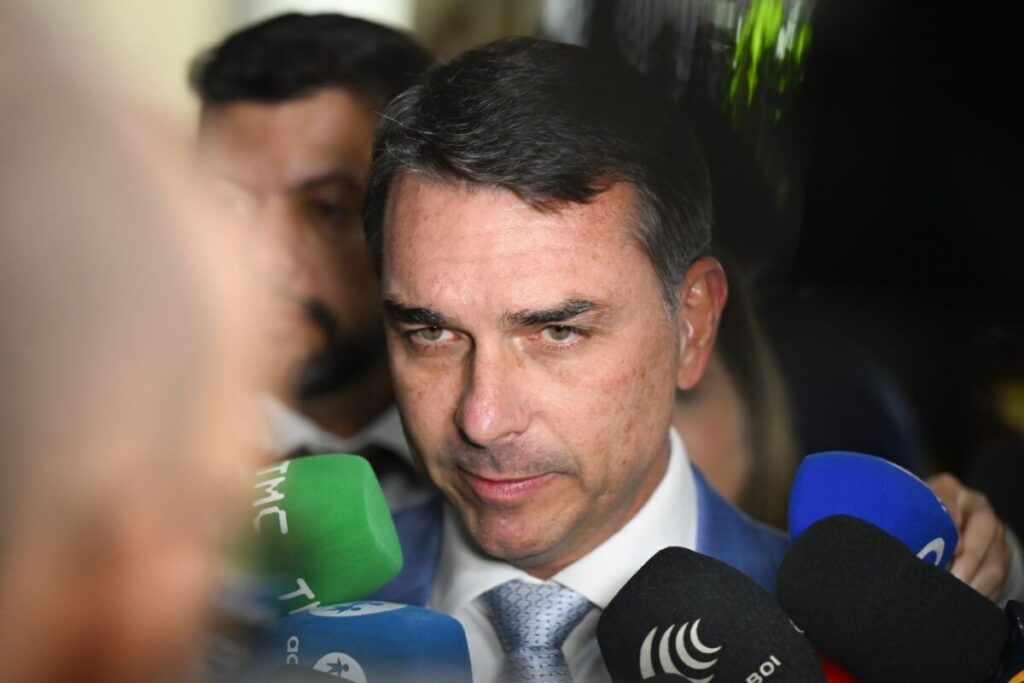 Close do senador Flávio Bolsonaro cercado de microfones de diferentes veículos durante uma entrevista