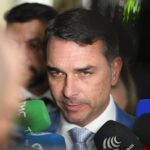 Close do senador Flávio Bolsonaro cercado de microfones de diferentes veículos durante uma entrevista