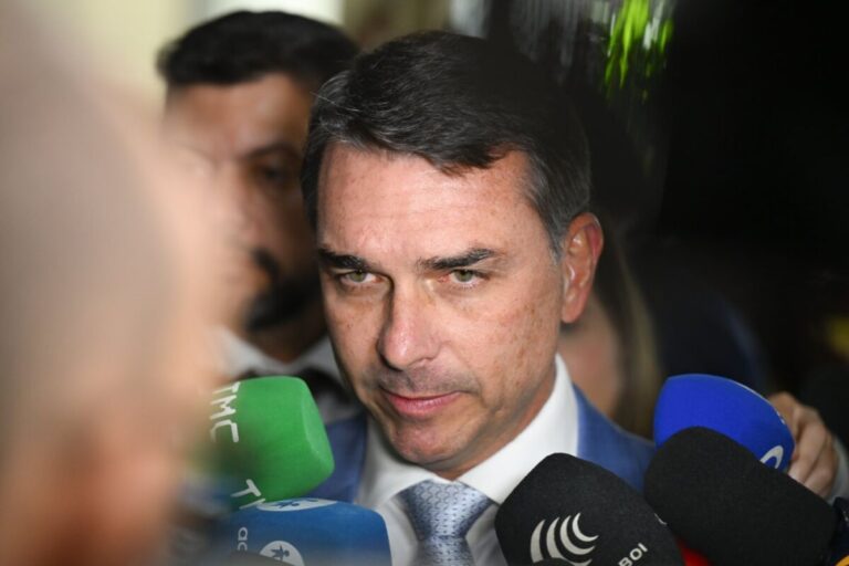 Close do senador Flávio Bolsonaro cercado de microfones de diferentes veículos durante uma entrevista