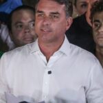 O senador Flávio Bolsonaro, de camisa branca, fala diante de aliados em pronunciamento, com camisetas amarelas ao redor