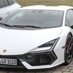 Lamborghini Revuelto branca estacionada, vista de frente e de lado, ao lado de outro carro