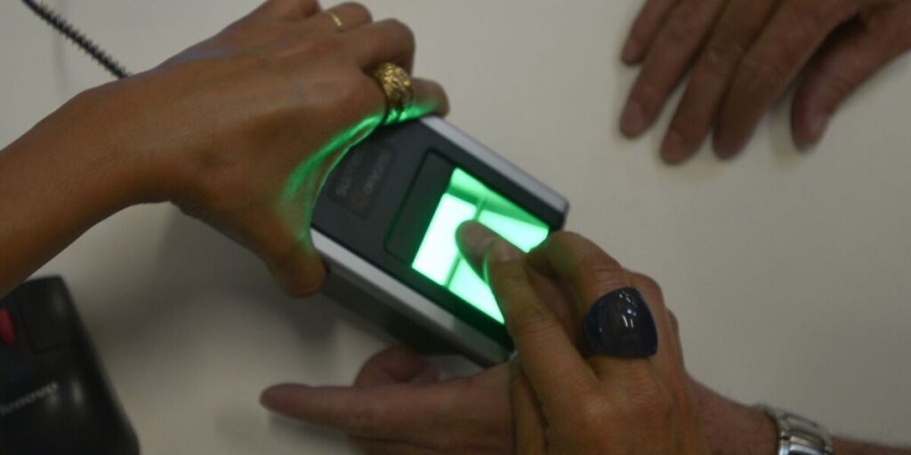 Mão posicionada sobre um leitor biométrico de impressões digitais com luz verde