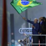 Lula acena com uma bandeira do Brasil em cima de um palanque, à noite, cercado de aliados, na Avenida Paulista