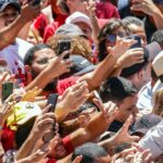 Lula, de chapéu claro, se inclina para cumprimentar apoiadores que erguem celulares e as mãos na festa da vitória