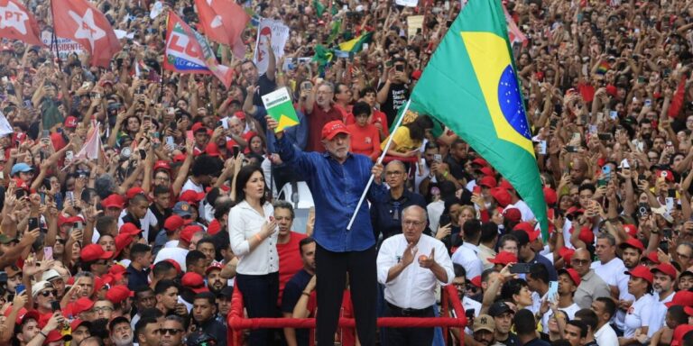 Lula acena com uma bandeira do Brasil diante de uma multidão vestida de vermelho, com bandeiras do PT, em ato na Avenida Paulista