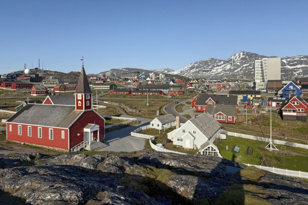 Vista de Nuuk, na Groenlândia, com a catedral de madeira vermelha, casas coloridas e montanhas com neve ao fundo