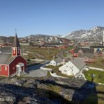 Vista de Nuuk, na Groenlândia, com a catedral de madeira vermelha, casas coloridas e montanhas com neve ao fundo