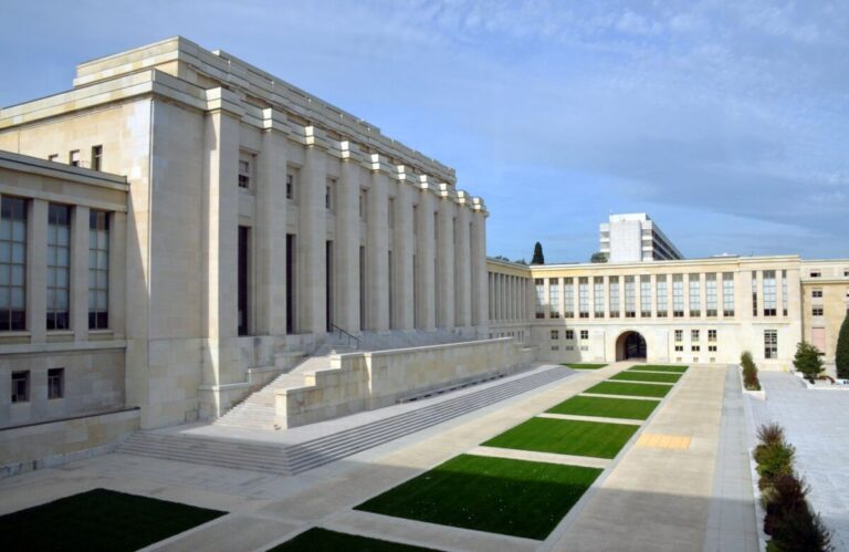 Fachada do Palácio das Nações, sede do escritório da ONU em Genebra, com bandeiras e jardim