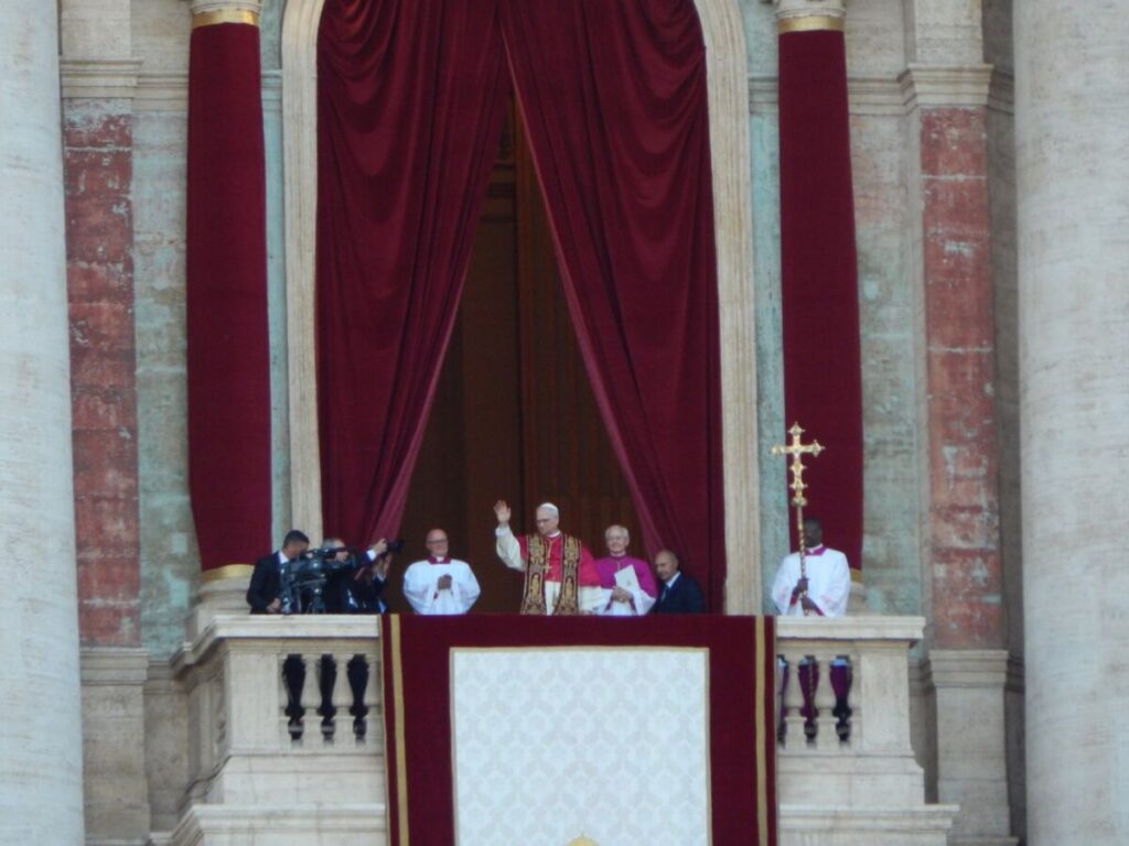 O papa Leão XIV acena da sacada da Basílica de São Pedro, ao lado de outros religiosos, em sua primeira aparição como papa
