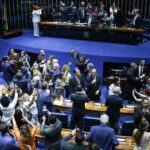 Plenário do Senado em momento de comemoração após a votação, com parlamentares de pé e fotógrafos no centro