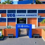 Fachada do Câmpus Sudoeste da Universidade Estadual de Goiás (UEG), em tijolo aparente com detalhes azuis, e totem de sinalização da UEG em primeiro plano.